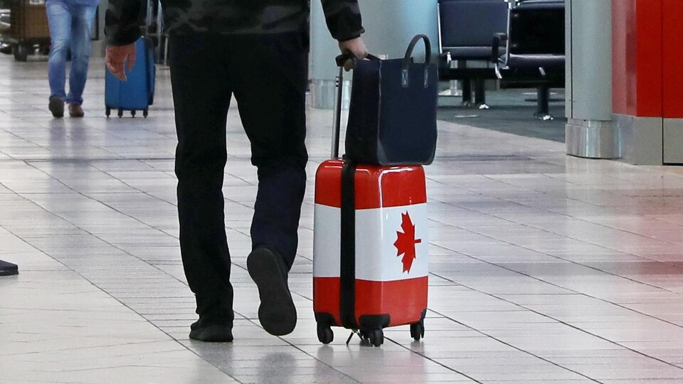 Un homme avec des écouteurs sur les oreilles tire une valise décorée des couleurs du drapeau du Canada.
