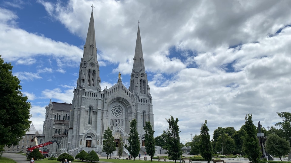 Exterior view of the facade of the Basilica of Saint-Anne-de-Beaupré under a blue and cloudy sky in summer.