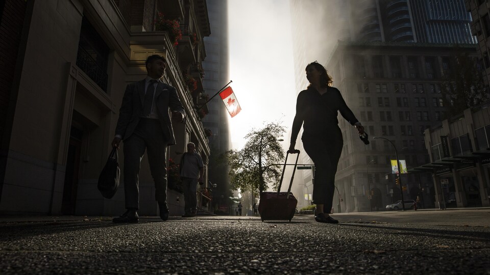 Des gens marchent au centre-ville de Vancouver. Une femme tire une valise.