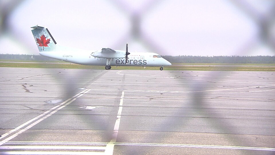 Un avion sur la piste d'atterrissage de l'aéroport de Sept-Îles photographié de la bordure de la piste à travers la clôture.
