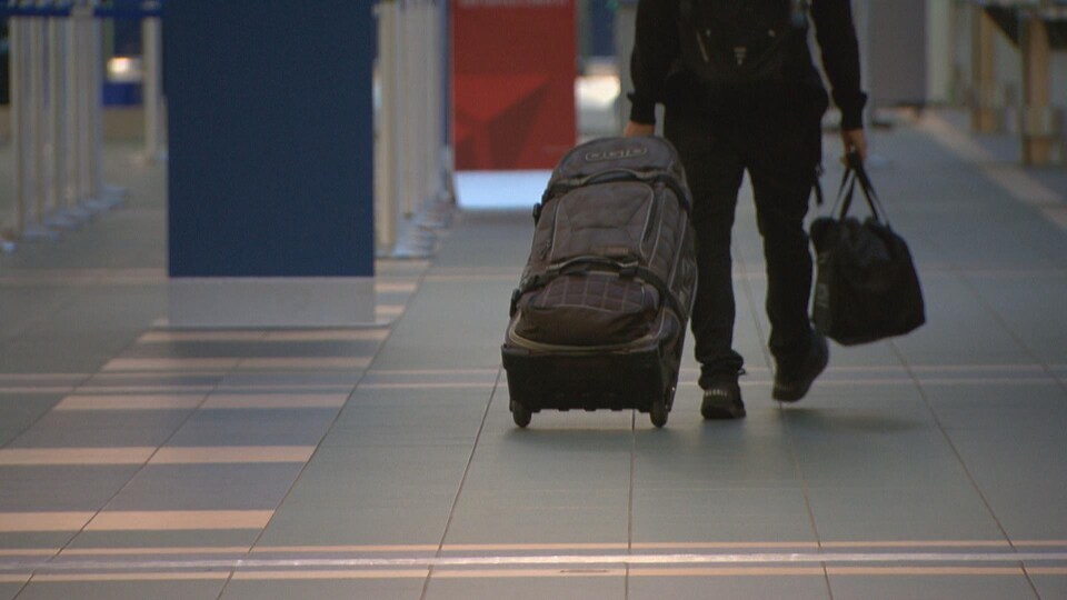 Un voyageur avec un petit sac à dos tire sa valise dans un hall d'aéroport.