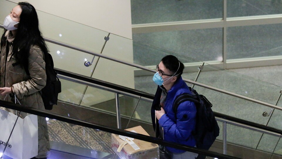 Deux voyageurs en provenance de Chine et portant des masques sont debout sur un escalier mécanique à l'aéroport de Seattle.