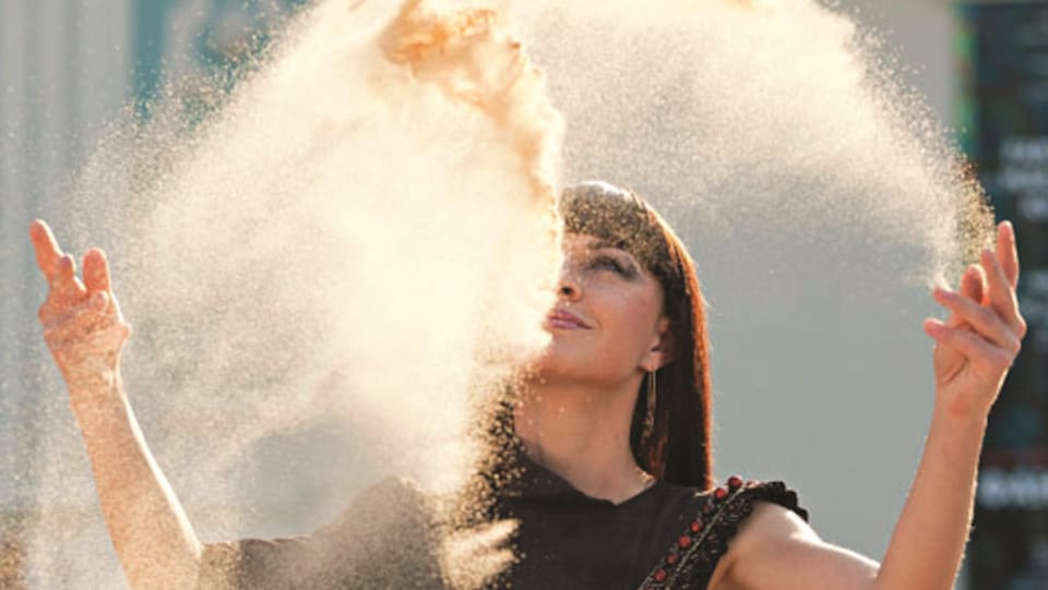 une femme projette du sable en l'air avec ses mains.