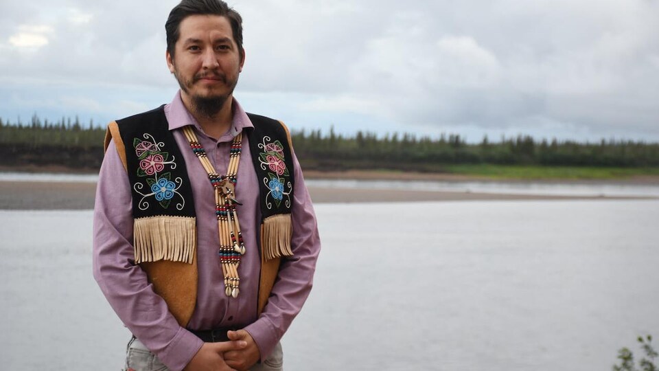 Un homme portant une veste d'inspiration autochtone se tient devant une rivière.