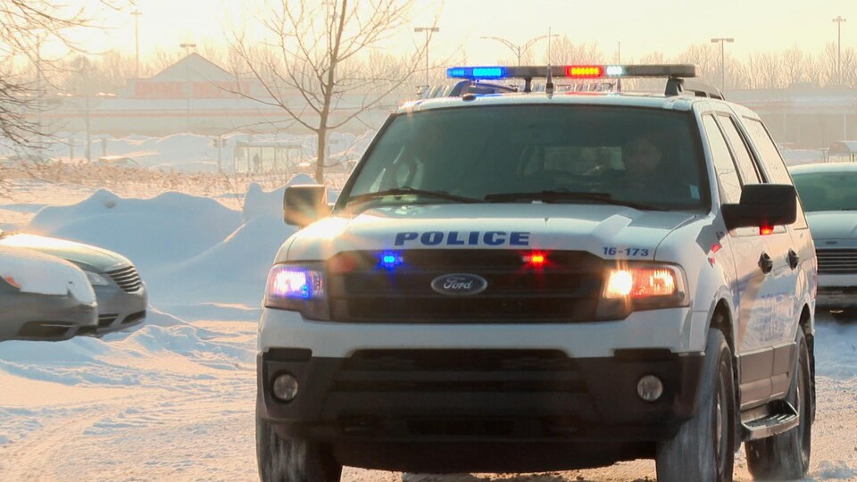 Un VUS de la police de Lévis, dont les gyrophares sont allumés, circule dans un stationnement, en hiver.