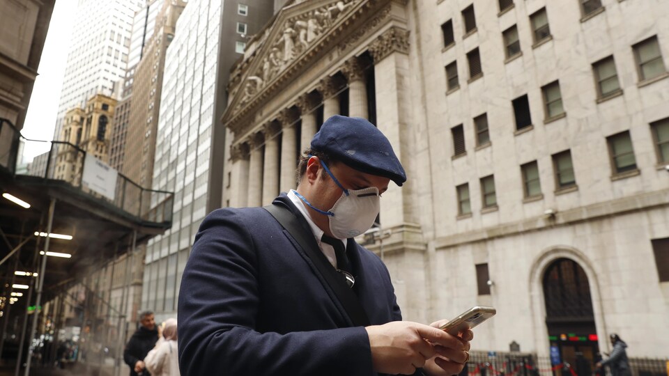 Un homme masqué consulte son téléphone cellulaire en pleine rue.