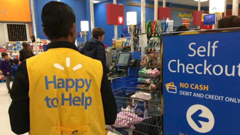 Un employé de Walmart observe des clients qui utilisent des caisses libre-service.