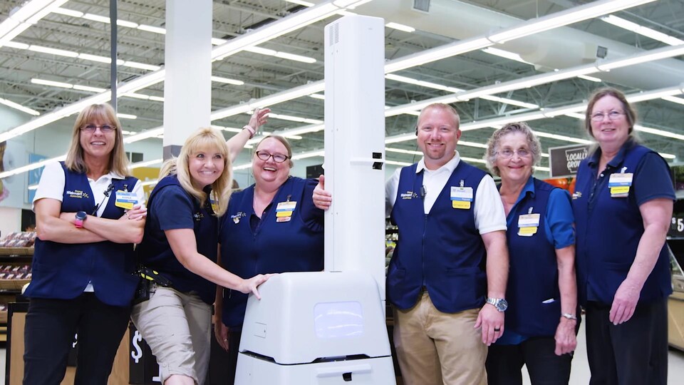 Des employés de Walmart posent autour d'un petit robot blanc en forme de boîte.