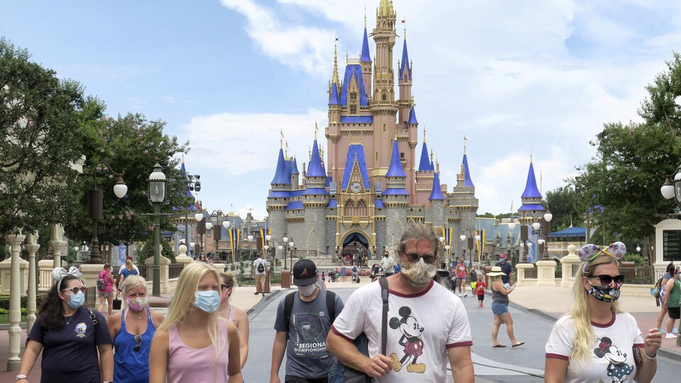 Des gens masqués marchent devant le château emblématique du parc d'attractions.