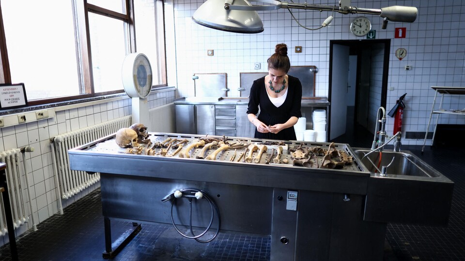 Mathilde Daumas devant une table d'examen où se trouvent des crânes et des os.