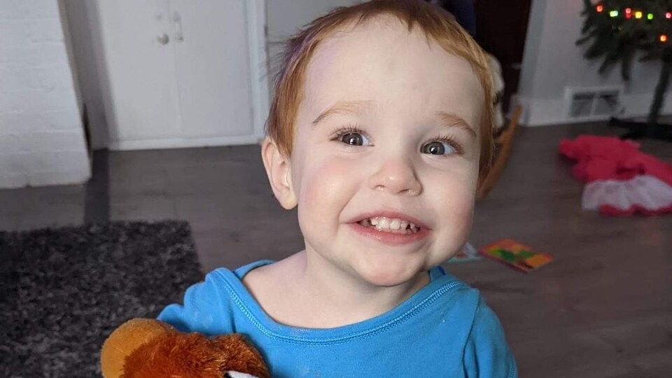 Portrait d'un petit garçon souriant. Il tient un ourson en peluche dans ses bras.