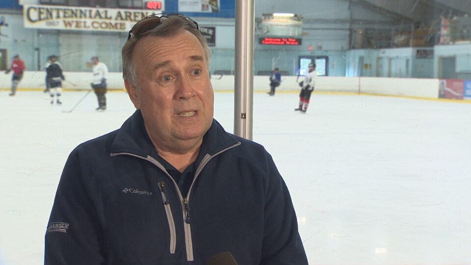 A father in an arena, his back to the bay window.  Behind him, the players have hockey practice.