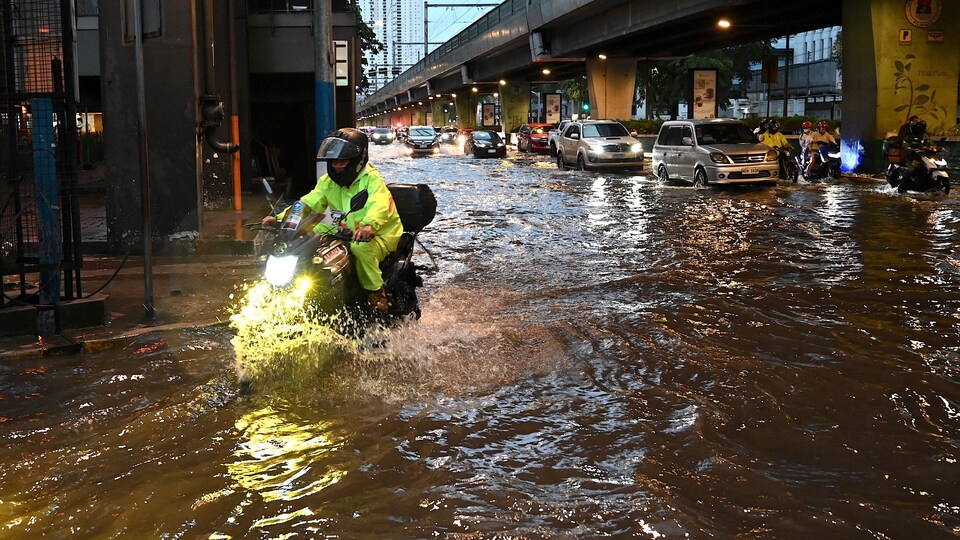 Des véhicules circulent sur une rue inondée de la capitale philippine. 