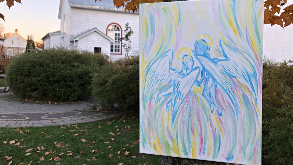 Une toile représentant deux anges est accrochée à un arbre.