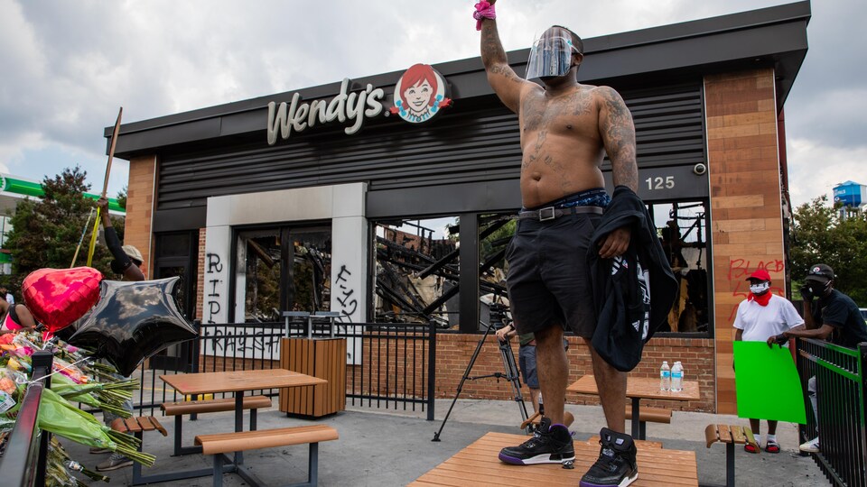 Un homme noir levant le poignet devant le restaurant calciné.