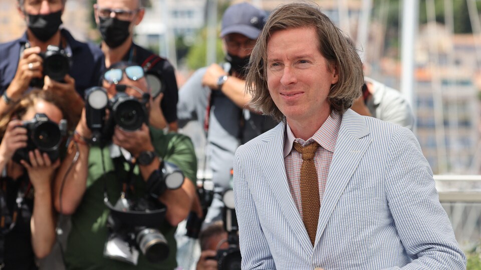 Un homme en veston cravate pose pour des photographes.