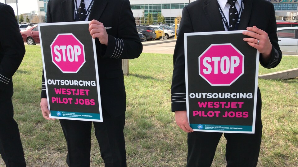 Des personnes qui tiennent une pancarte dans leurs mains sur laquelle il est écrit: Stop, outsourcing westjet pilot jobs