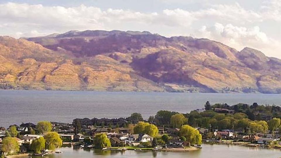 Vue aérienne de maisons devant un lac et des montagnes.