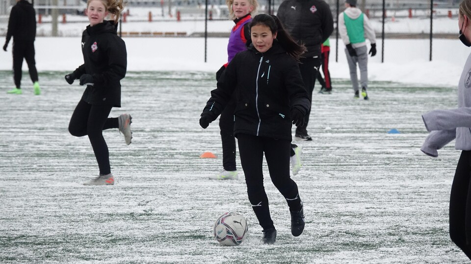 Une jeune joueuse contrôle un ballon de soccer sur un terrain enneigé.