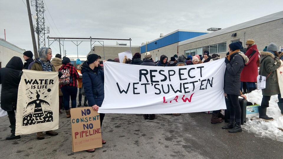 Des manifestants tiennent un drapeau où il est écrit "Respectez al loi Wet'suwet'en" et "Pas de consentement, pas de pipeline".