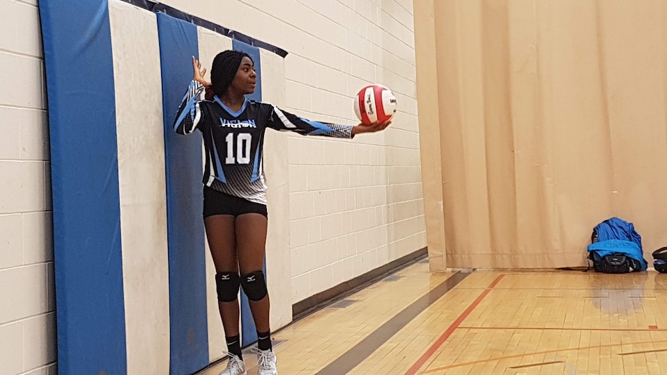 Whitney Ashu est photographiée dans un gymnase alors qu'elle s'apprête à faire un service au volleyball.