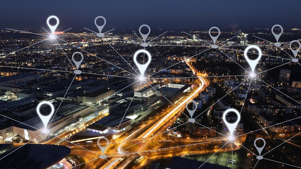 Un paysage urbain photographié de nuit sur lequel a été superposé un réseau de lignes représentant un réseau Internet.