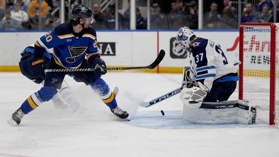 Le gardien des Jets Connor Hellebuyck arrête un tir de l'attaquant des Blues Brandon Saad.