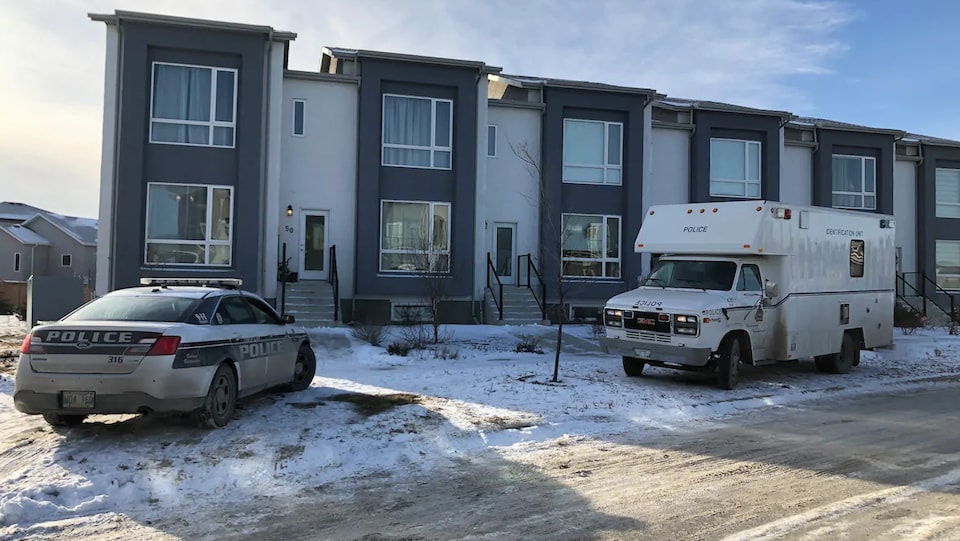Une résidence d'appartements avec un camion de police et une voiture de police garés devant.