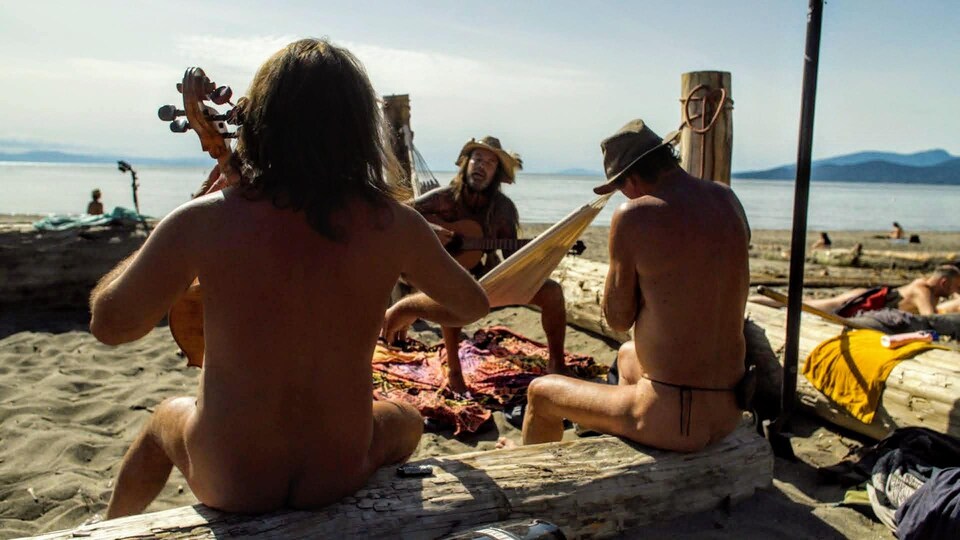 Trois hommes nus jouent de la musique sur la plage par beau temps.