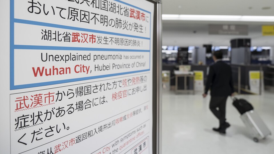 Un voyageur passe près d'une affiche écrite en anglais et en mandarin qui demande aux gens de déclarer leurs symptômes s'ils sont grippés.
