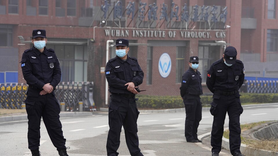On voit des policiers portant des masques chirurgicaux, devant un édifice où il est écrit Wuhan Institute of Virology.