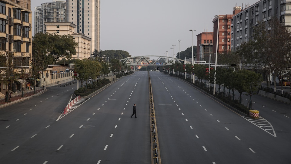 Un homme marche seul au milieu d'un boulevard urbain.