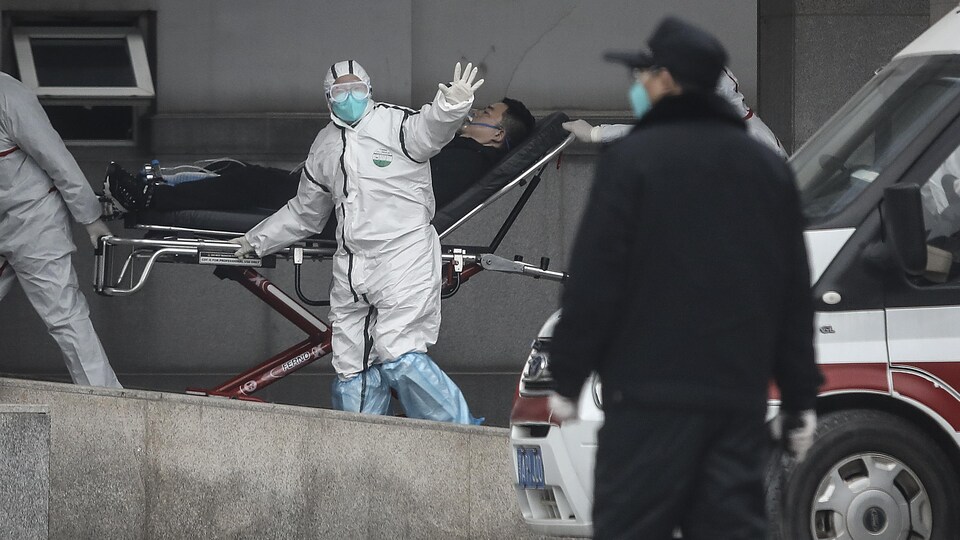 Un patient est transporté par le personnel médical en tenue de protection.