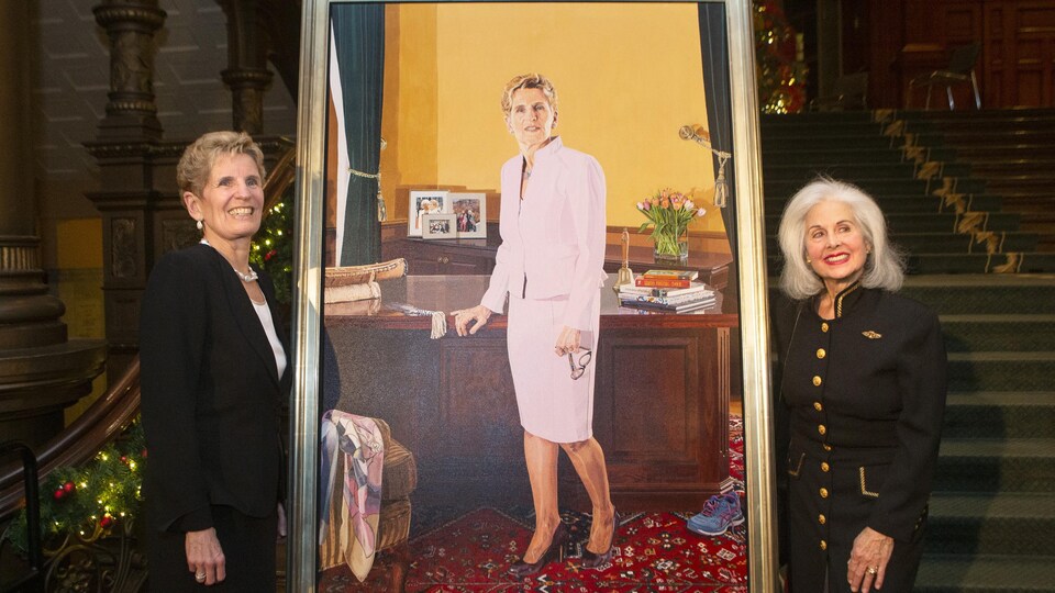 Deux femmes prennent la pause à côté d'un portrait.