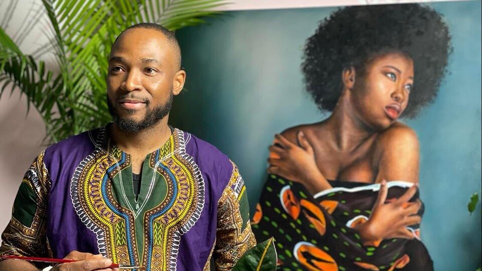 Pinceau à la main, Xavier Mutshipayi est devant un de ses tableaux représentant une femme s'enlaçant.