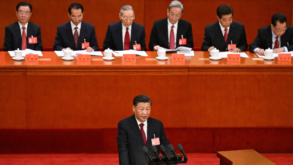 Chinese leader Xi Jinping delivers his opening speech at the Chinese Communist Party Congress to men seated behind him on the podium.