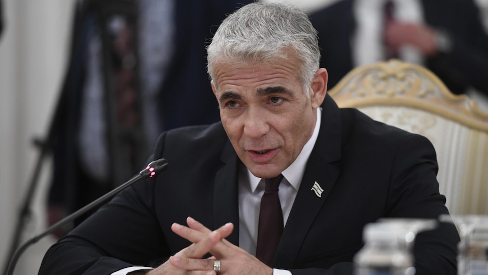 Yaïr Lapid est assis dans un fauteuil et parle dans un micro.