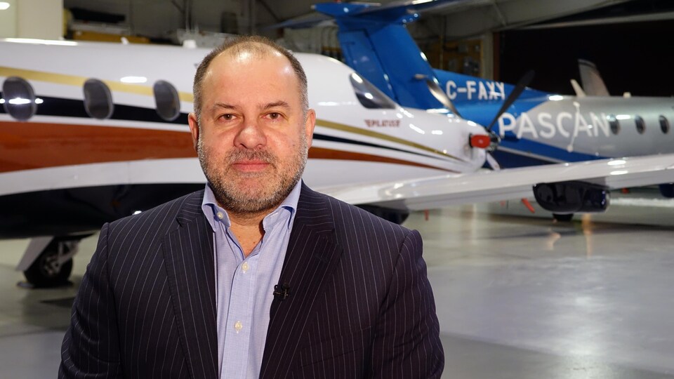 Un homme en complet se tient devant des avions dans un hangar.
