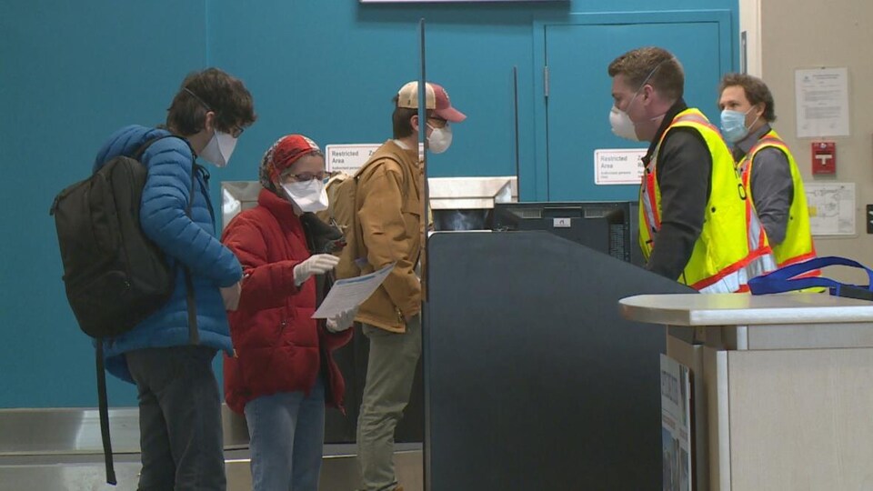 Des voyageurs portant un masque attendent en file à l'aéroport de Yellowknife.
