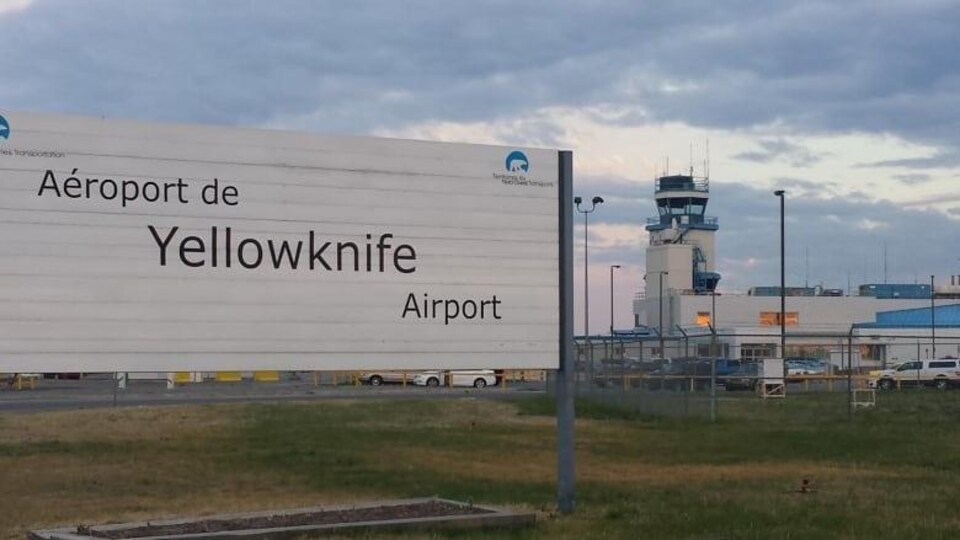 Une pancarte affichant l'aéroport de Yellowknife, avec en arrière-plan la tour de contrôle.