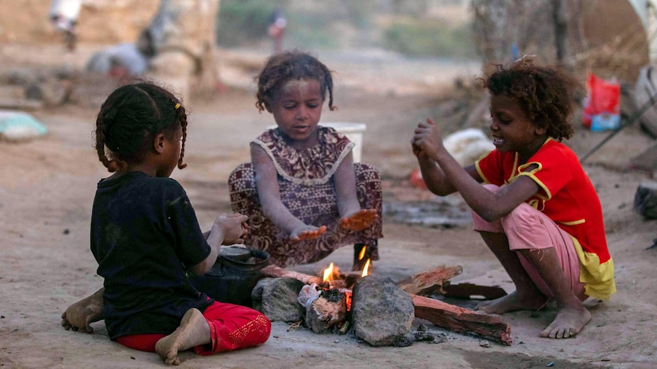 Trois enfants se réchauffent autour d'un feu.