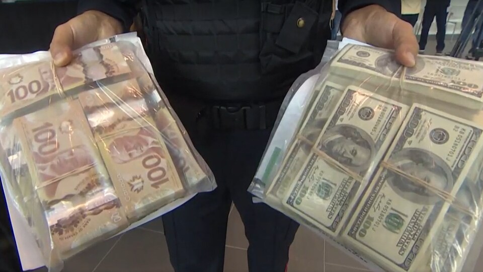 Un policier tient des sacs remplis de billets de 100 $ canadiens et américains.