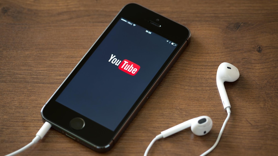 Le logo de YouTube est affiché sur un téléphone intelligent posé sur une surface en bois. 
