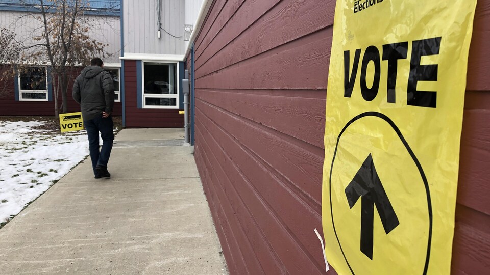 Un électeur se dirige vers l'entrée d'un lieu de scrutin marqué par des affiches.