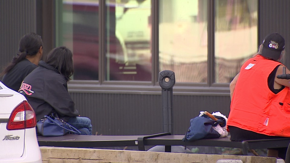 Des gens de dos assis sur un banc devant un édifice.