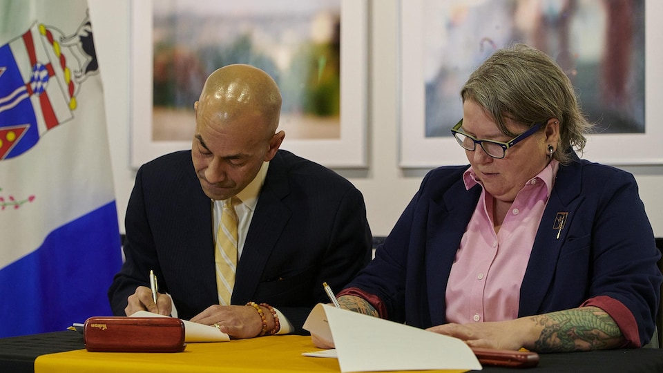 Ranj Pillai et Kate White signent un document devant un drapeau du Yukon.