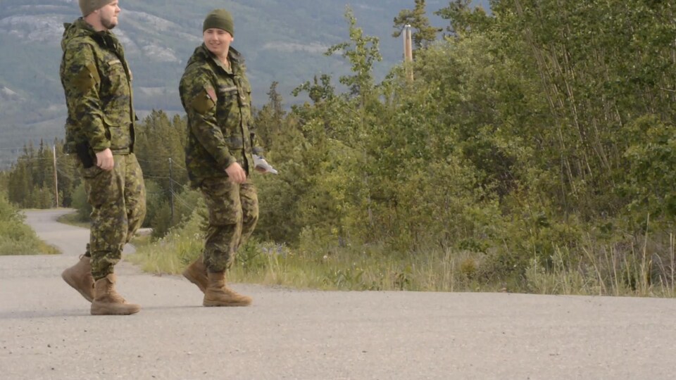 Deux soldats marchent sur une route bordée de forêt.