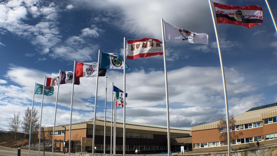 Les drapeaux des Premières Nations du Yukon flottent au vent sur des mâts installés devant un édifice.