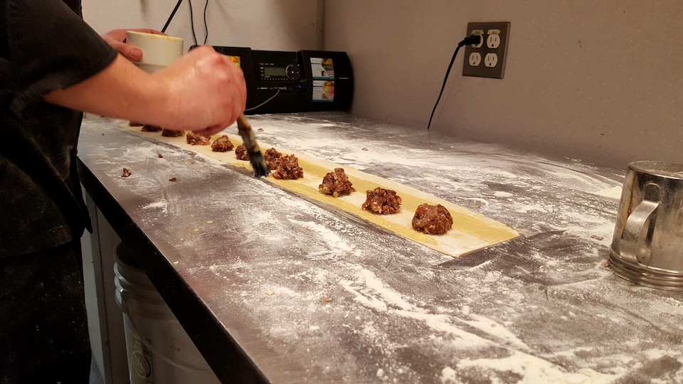 Un comptoir farineux sur lequel repose une lanière de pâte parsemée de boules de viande qui deviendront des raviolis.