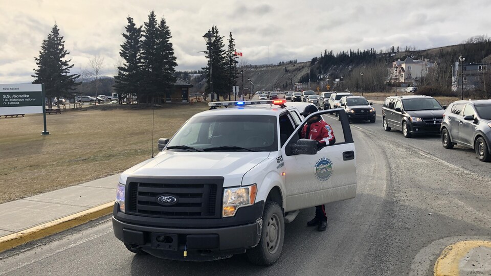 Une camionnette avec des gyrophares bloque l'entrée d'une voie de circulation devant une file de voitures.